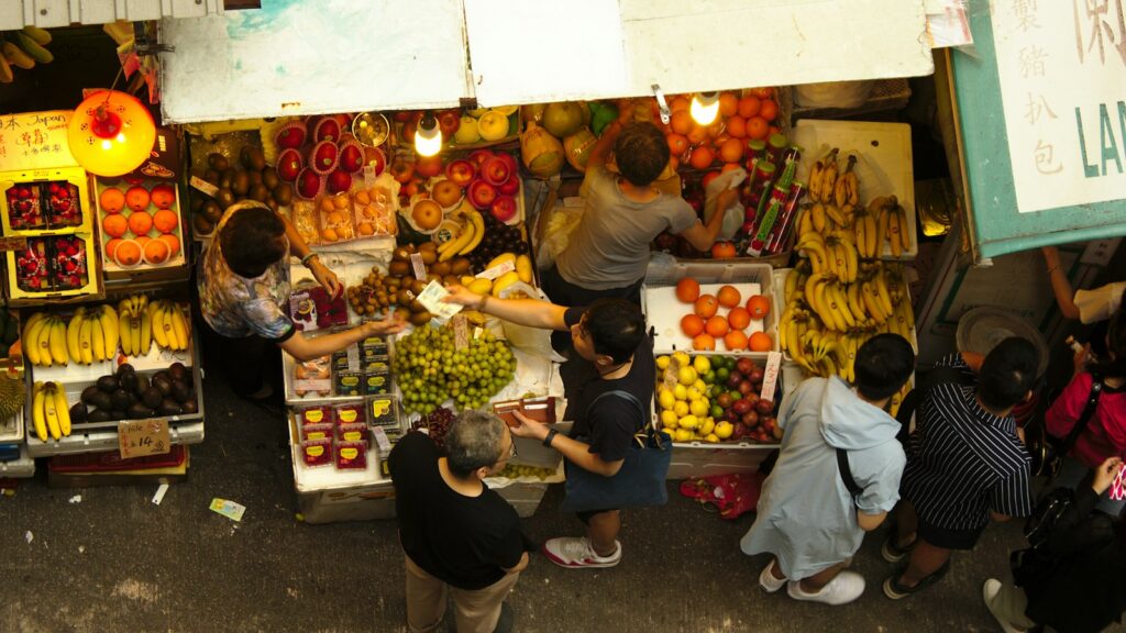 A street fruit and vegetable market seen from above, with shoppers and stallholders between the stalls