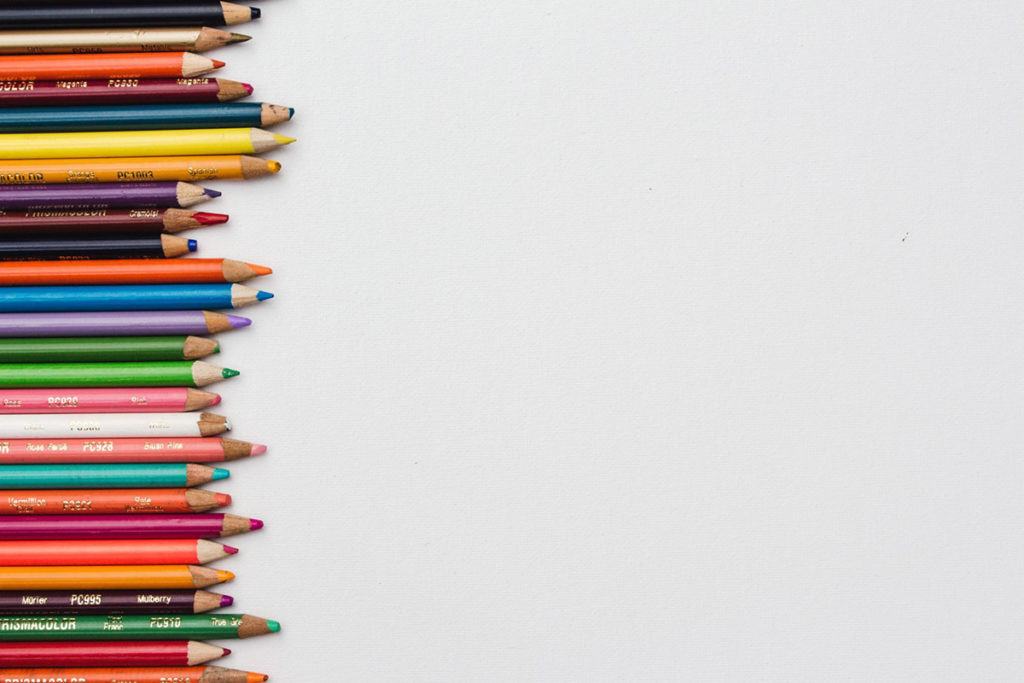 Sharpened coloured pencils lined up in a column down the left side of a plain white background